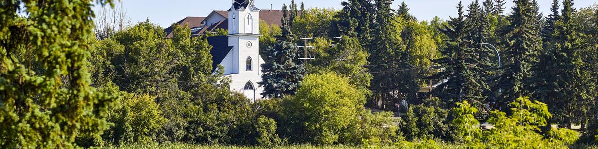 The white Ukrainian Catholic Church building reflected in a tranquil Mirror Lake surrounded with trees in the community of Camrose; Camrose, Alberta, Canada