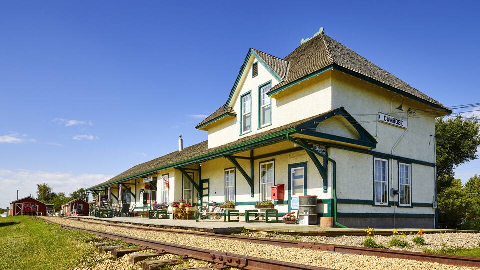 A train station with a white building, green trim, and a sign reading 'CAMROSE.'