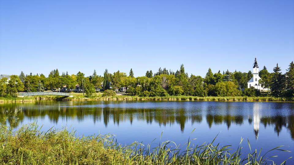 A calm lake with a bridge, surrounded by trees and a church.