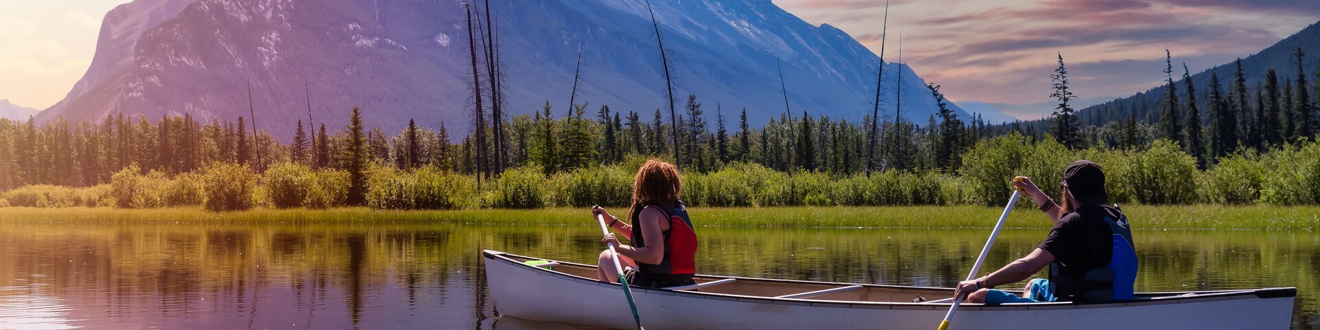 Couple adventurous friends are canoeing in a lake surrounded by the Canadian Mountains. Colorful Sunrise Sky Art Render. Taken in Vermilion Lakes, Banff, Alberta, Canada.