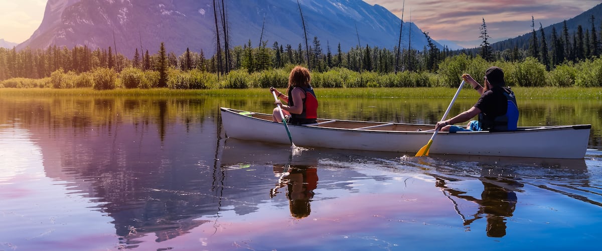 A canoe on a calm lake with mountains in the background.