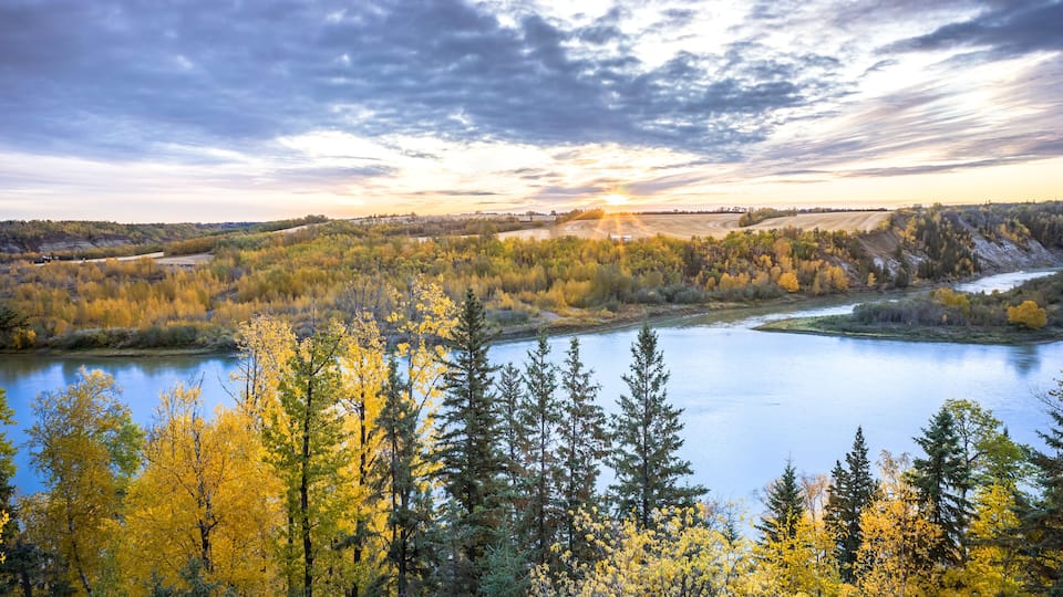 A river surrounded by autumn-colored trees and a cloudy sky.