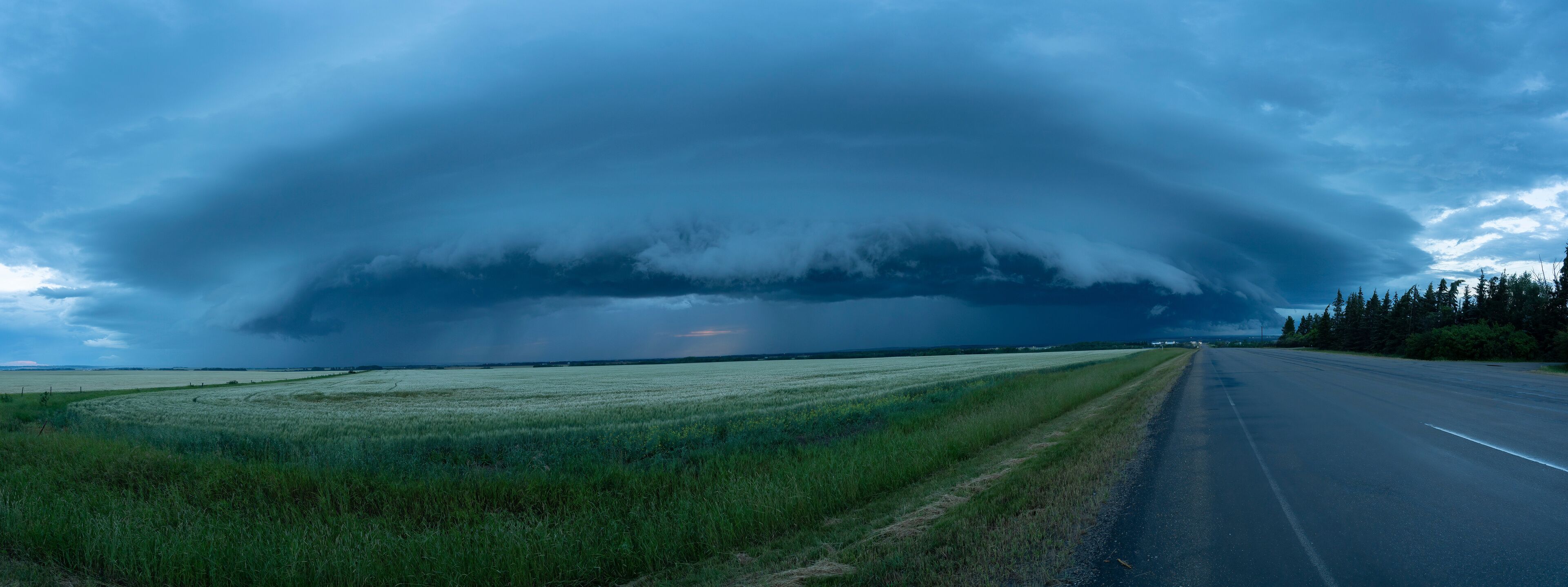 A road with a large storm cloud overhead.