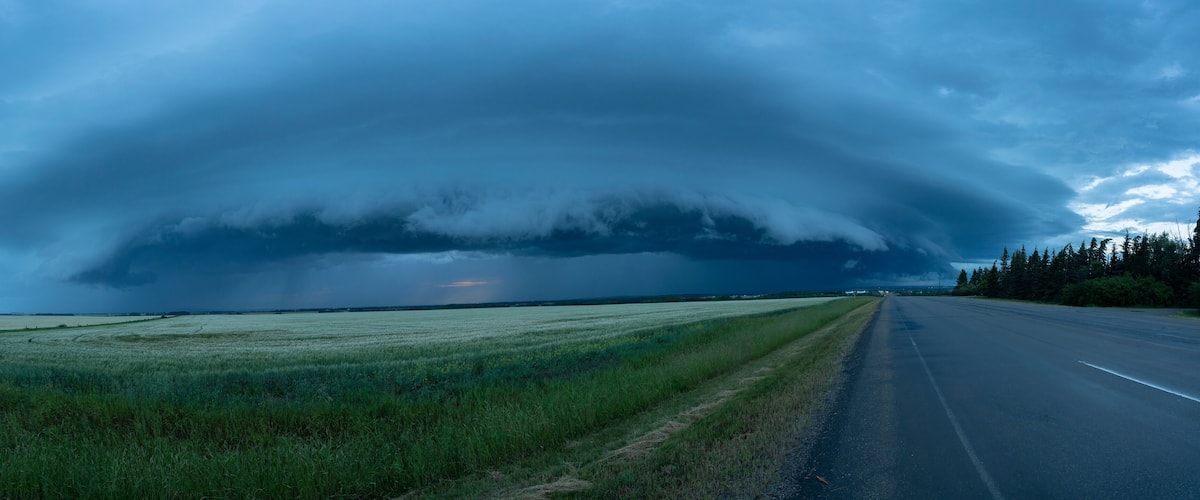 A road with a large storm cloud overhead.