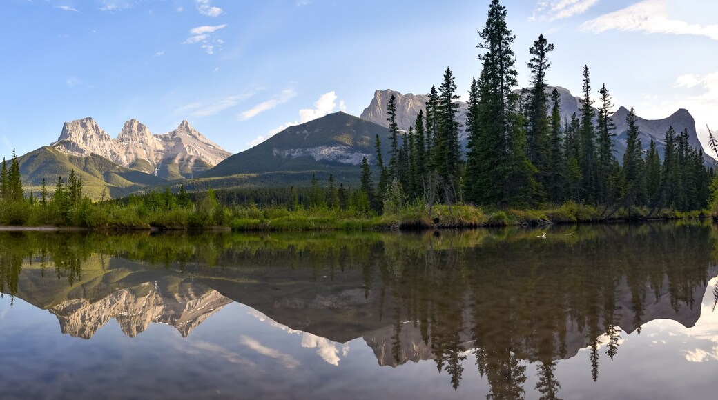 Three Sisters in Canmore seen at golden hour, sunset on blue sky day, afternoon with calm, peaceful reflection in water below famous, tourist, tourism mountains, area summer.