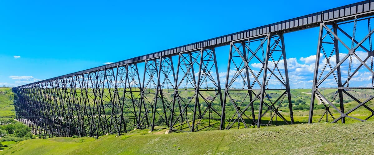 A large steel bridge spanning a valley with green hills and a clear blue sky.