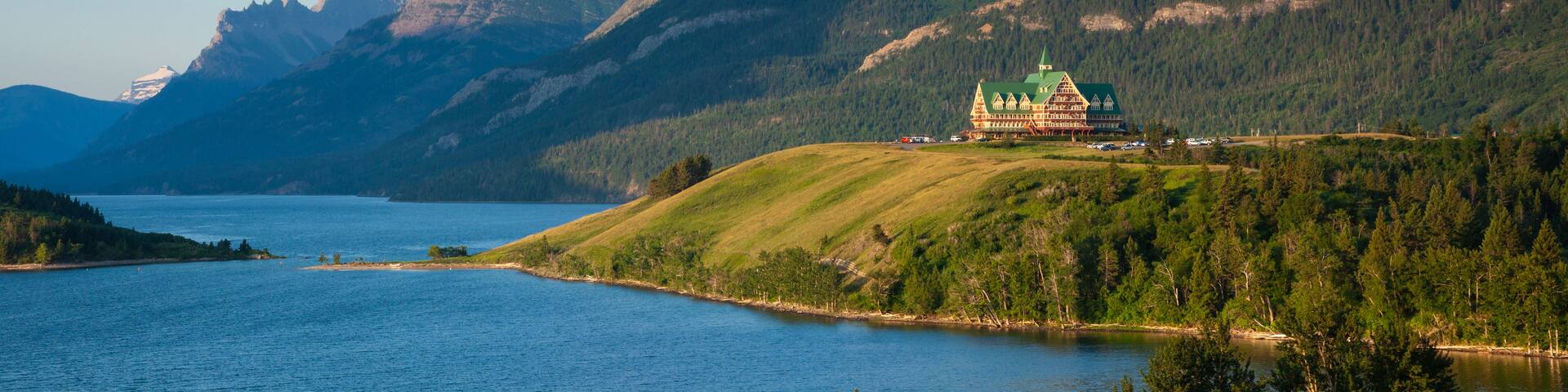 Un lac entouré de montagnes, un bâtiment à toit végétalisé perché sur une colline et un ciel bleu azur.