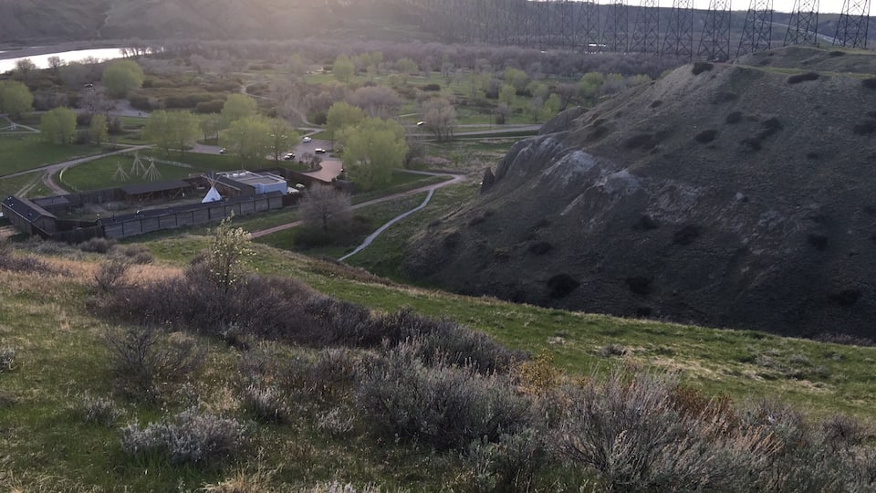 A hilly landscape with a large rock formation, a bridge, and a building complex.