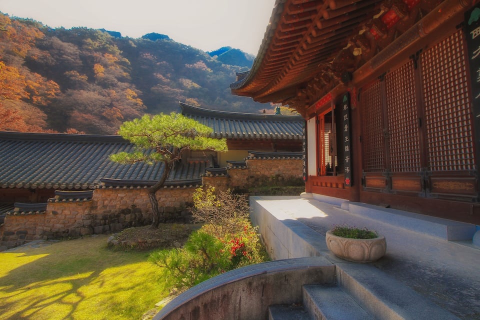 Un templo coreano tradicional con muros de piedra, tejados de tejas y una escalera de piedra que conduce a la entrada.