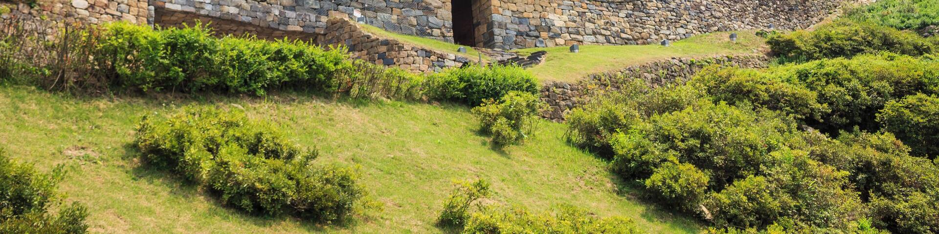 A traditional Korean fortress with stone walls and a tiled roof, surrounded by lush greenery and trees.