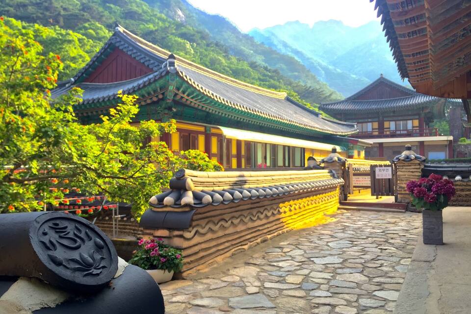 A traditional Korean temple with ornate architecture, surrounded by lush greenery and mountains.