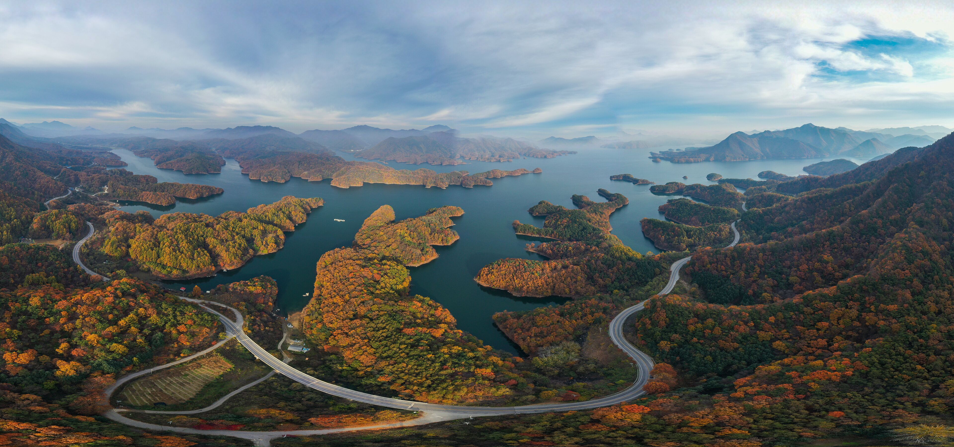 A winding road through a mountainous landscape with a lake surrounded by autumn-colored trees.