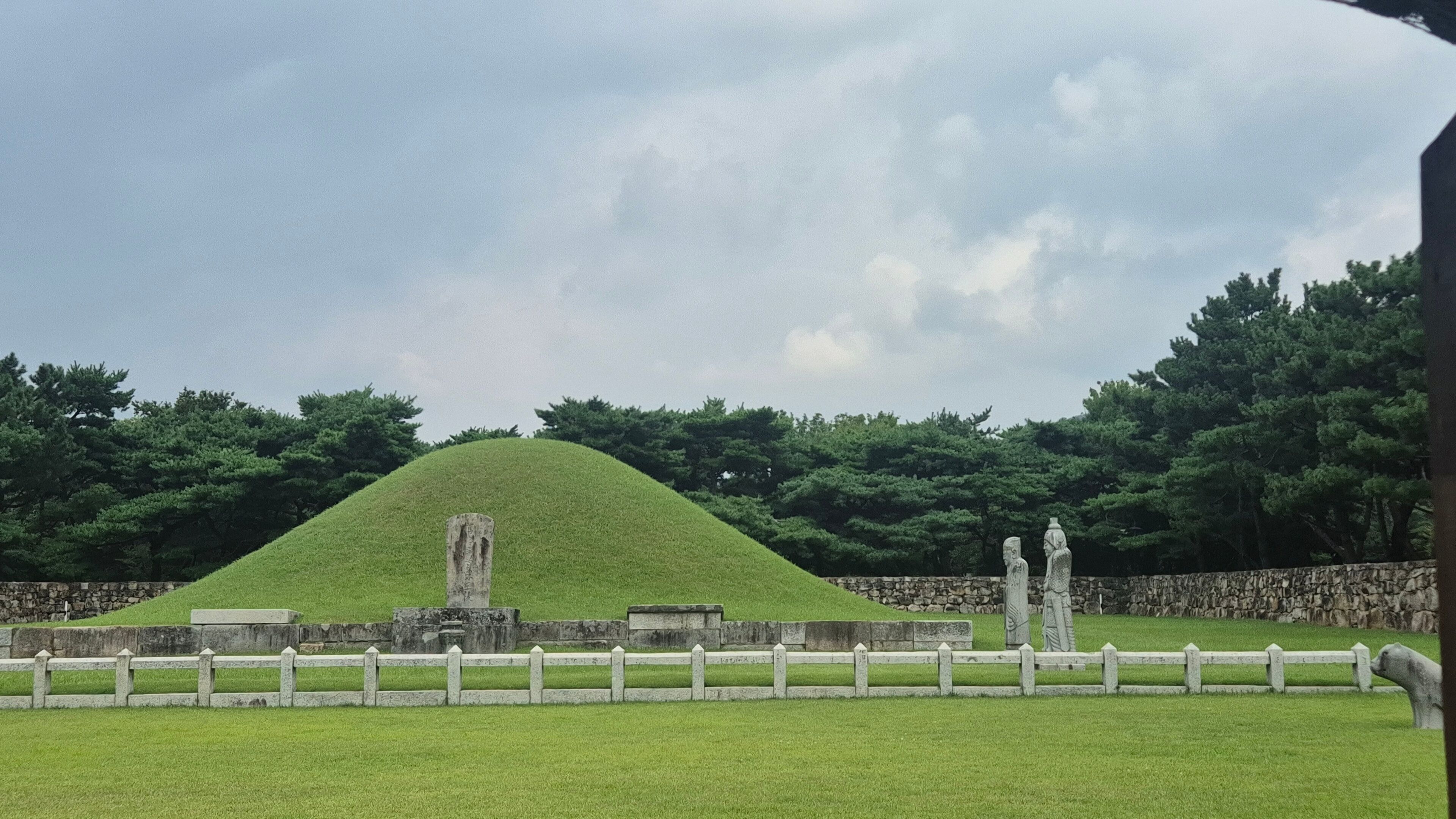 Ancient royal tomb of King Suro in Gimhae, South Korea, with grassy burial mound, stone statues, and historical landscape surrounded by pine trees