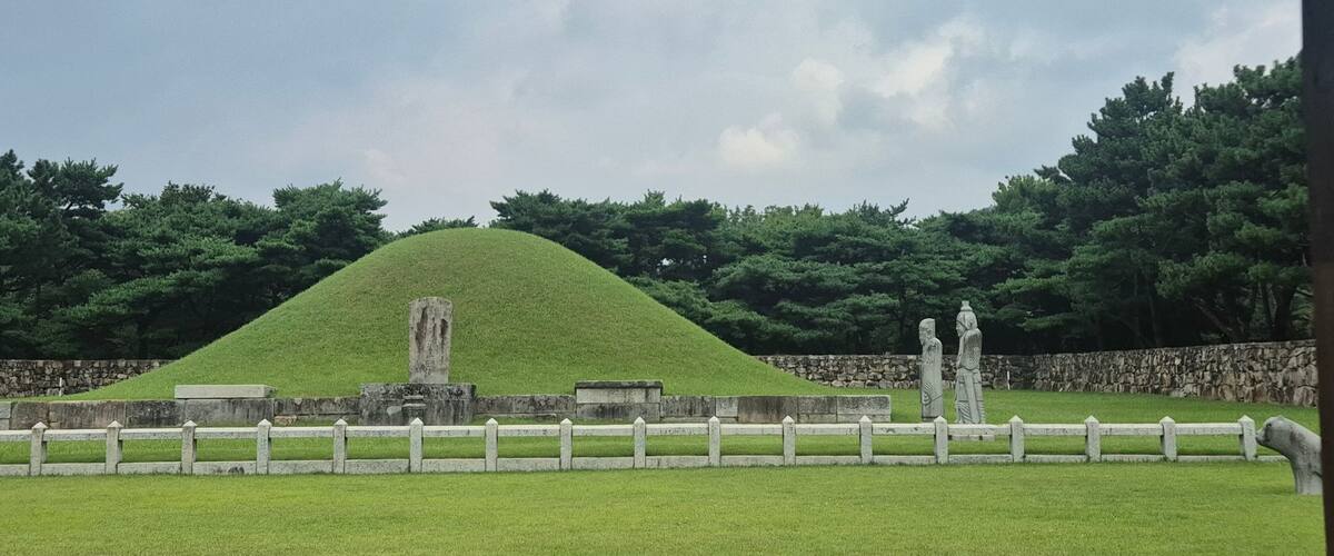 Ancient royal tomb of King Suro in Gimhae, South Korea, with grassy burial mound, stone statues, and historical landscape surrounded by pine trees
