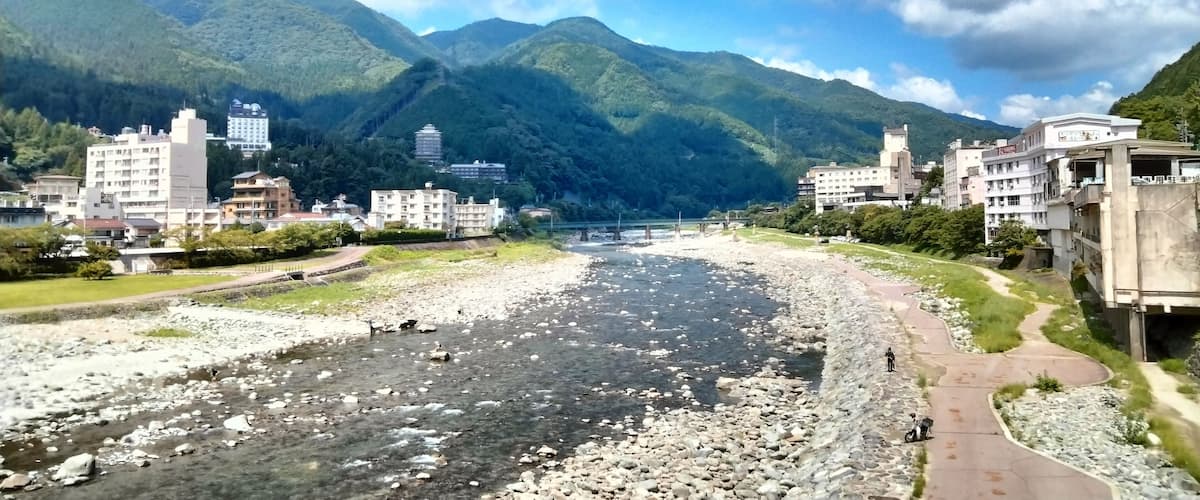 A river with rocks, a bridge, and mountains in the background.