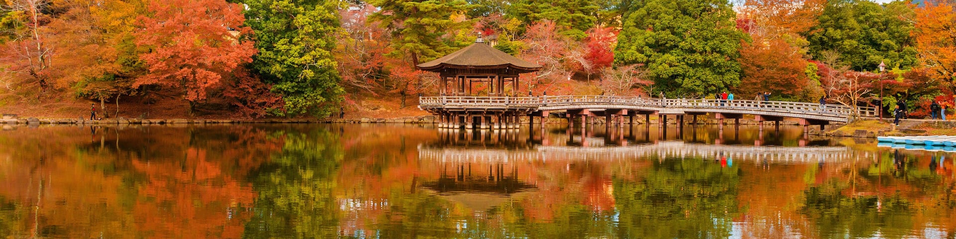 Scenic view of Nara public park in autumn, with maple leaves, pond and old oriental pavilion reflected in the water