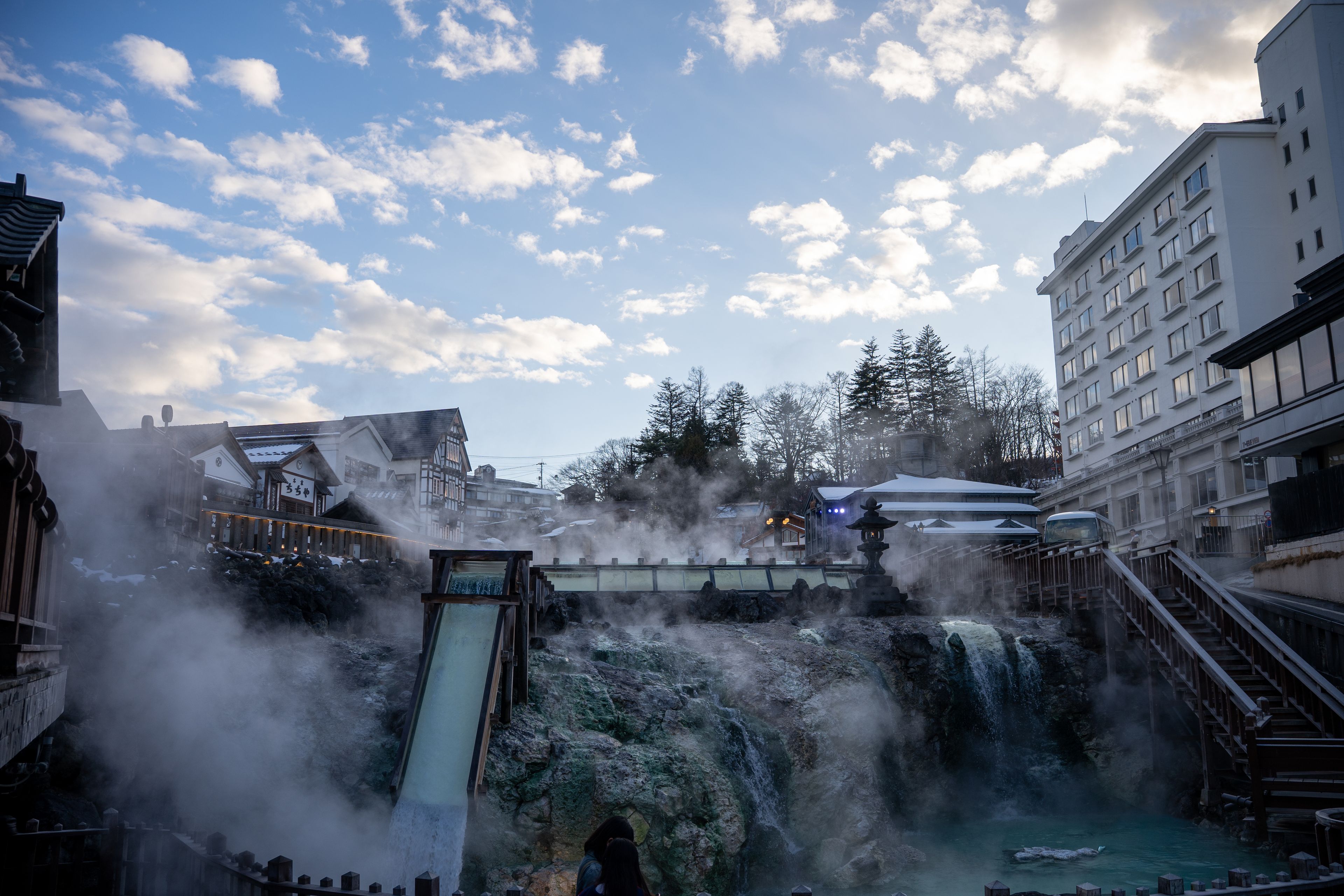 A waterfall with steam, a wooden slide, and traditional buildings.