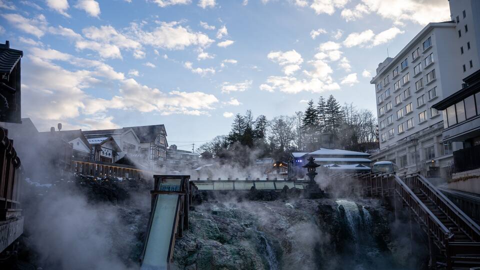 A waterfall with steam, a wooden slide, and traditional buildings.