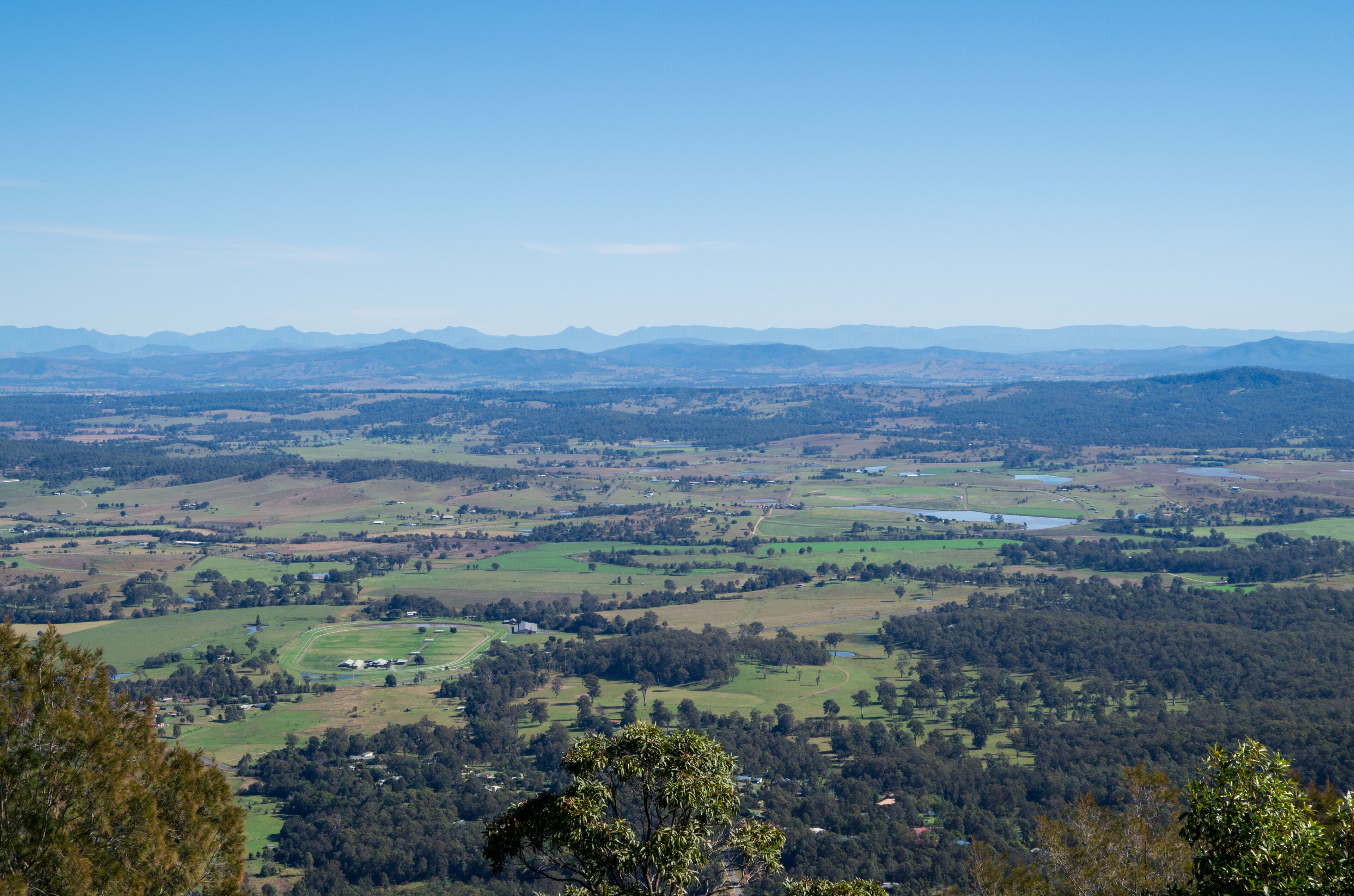 A panoramic view of a valley with rolling hills, scattered trees, and distant mountains under a clear sky.