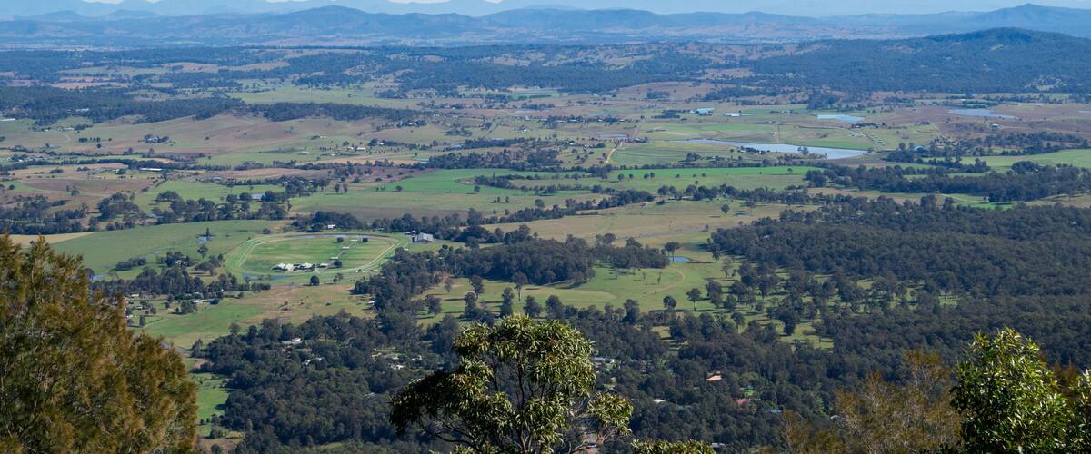 A panoramic view of a valley with rolling hills, scattered trees, and distant mountains under a clear sky.