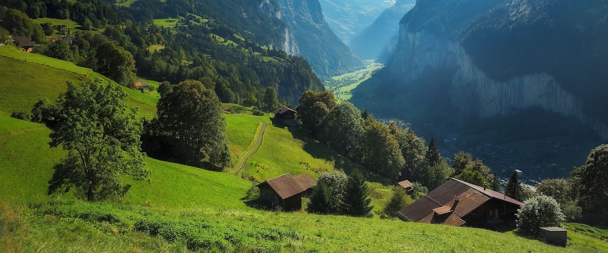 A mountainous landscape with snow-capped peaks, green valleys, and traditional houses.