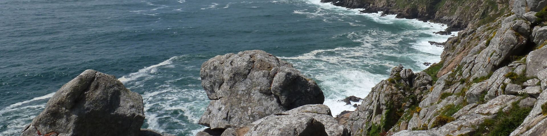 A rocky coastline with waves crashing against the shore and a clear sky above.