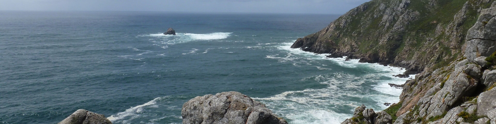 Costa rocosa con olas rompiendo en la orilla y un cielo despejado.