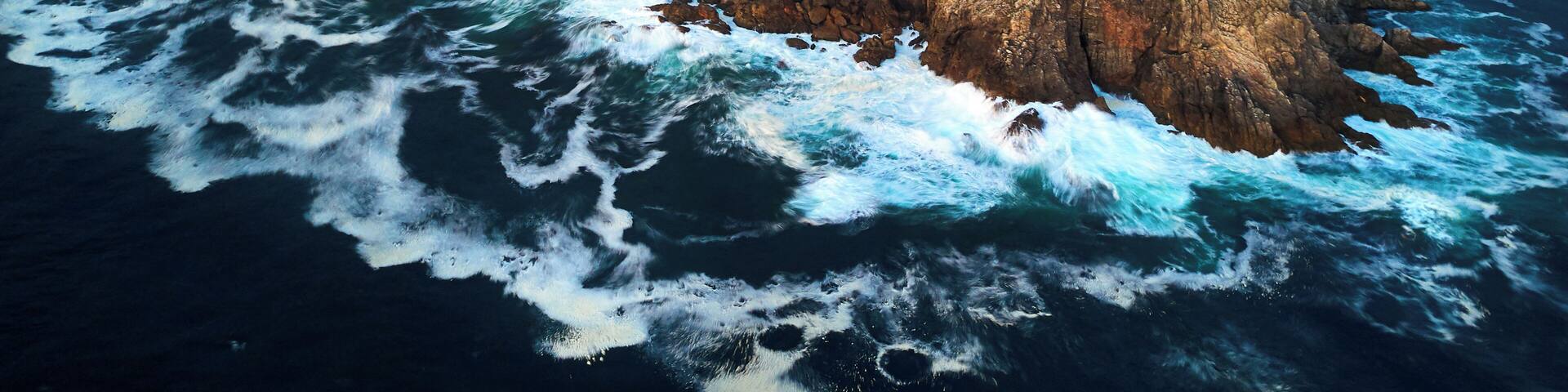 A rocky coastline with waves crashing against it and a building on the cliff.