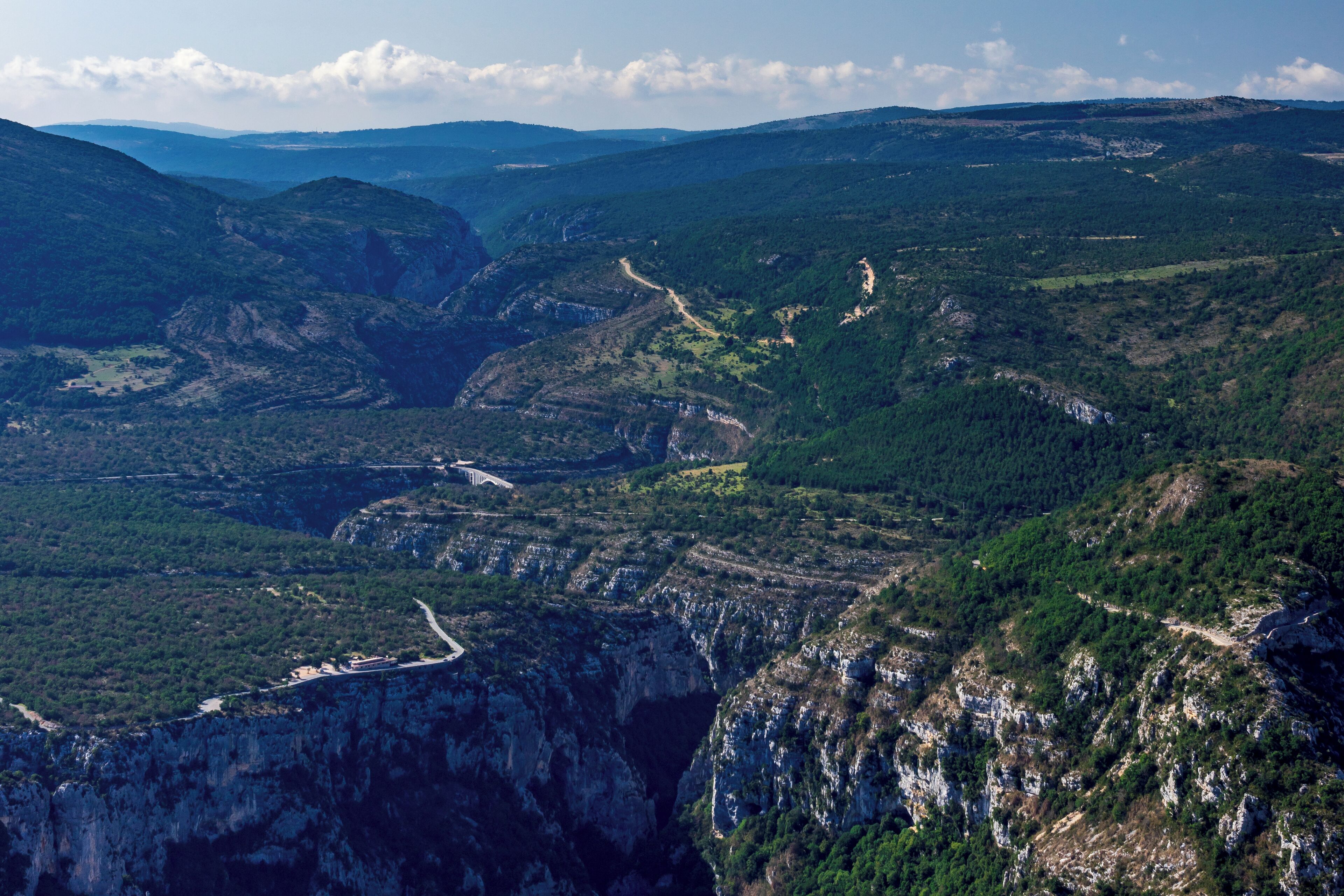 A mountainous landscape with a winding road, steep cliffs, and dense forests.