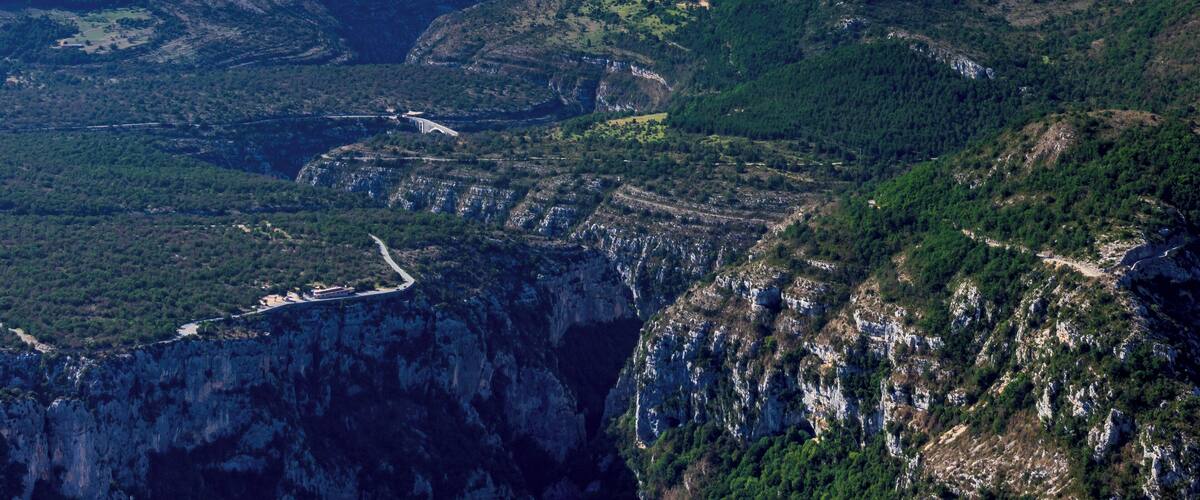 A mountainous landscape with a winding road, steep cliffs, and dense forests.
