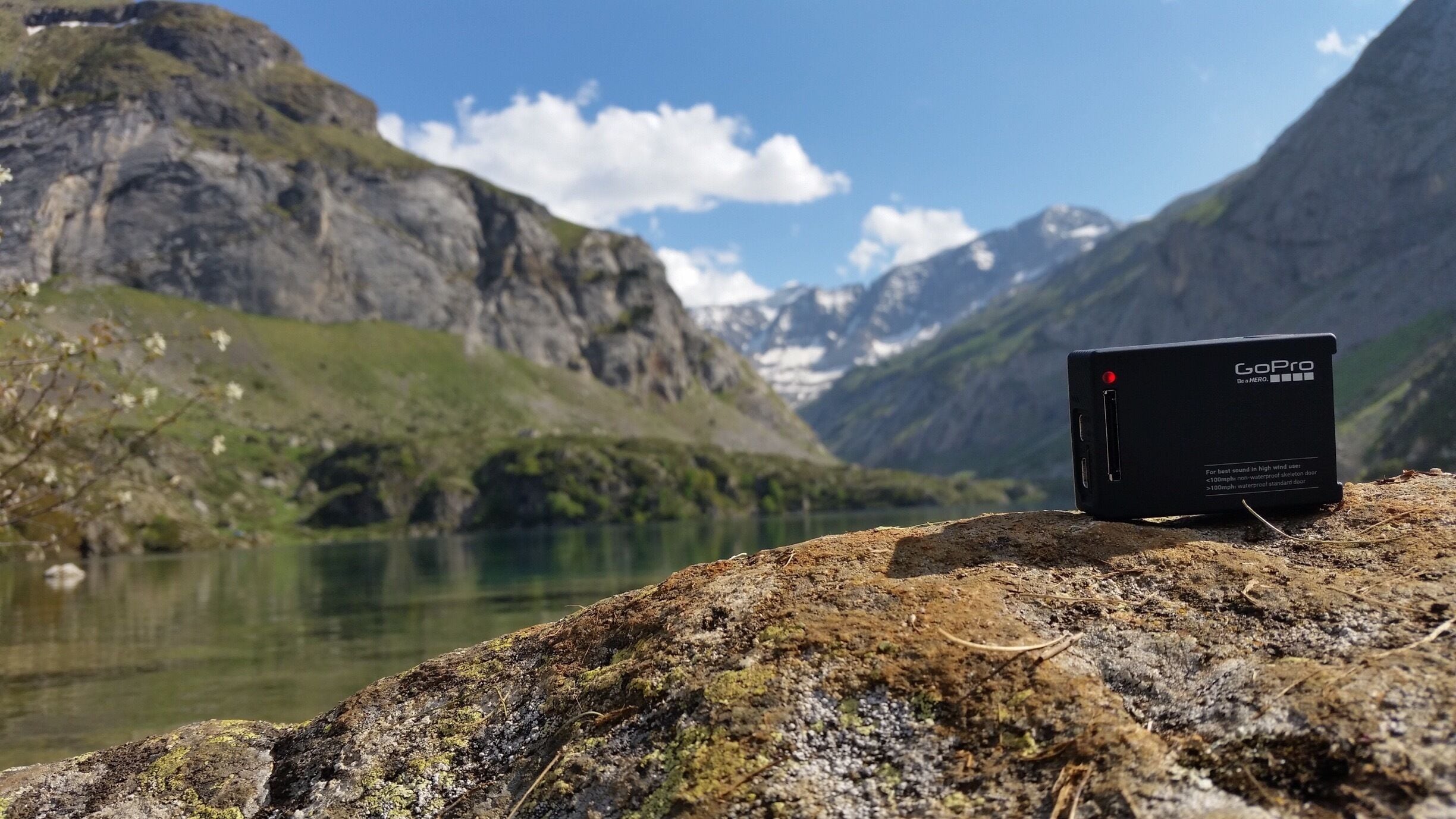 A GoPro camera on a rock by a lake with mountains in the background.