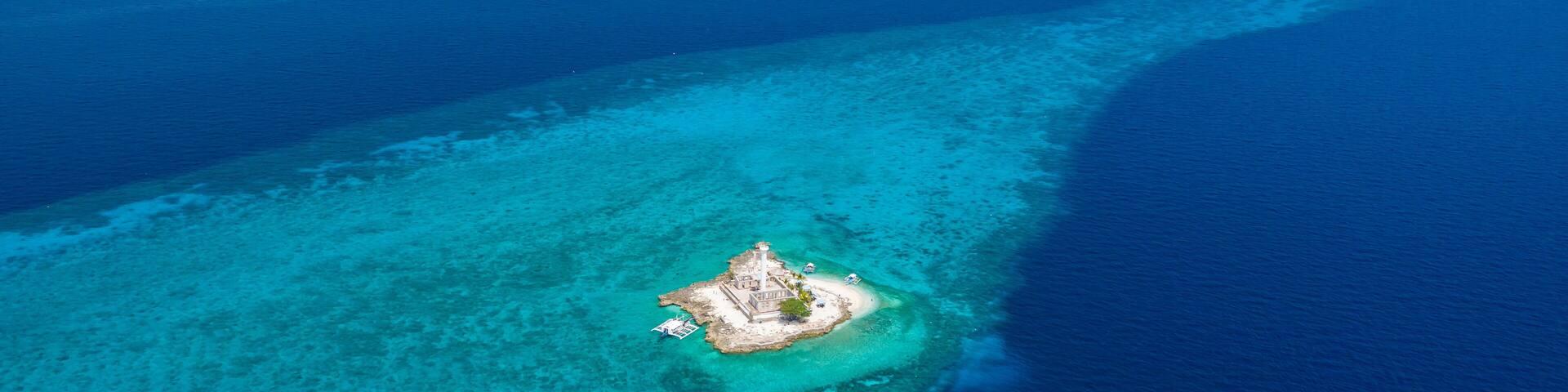 Aerial drone view of tropical Capitancillo Island in the Philippines showing its lighthouse and coral reef