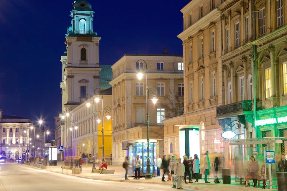 A nighttime city street with historic buildings, a clock tower, and a tram stop.