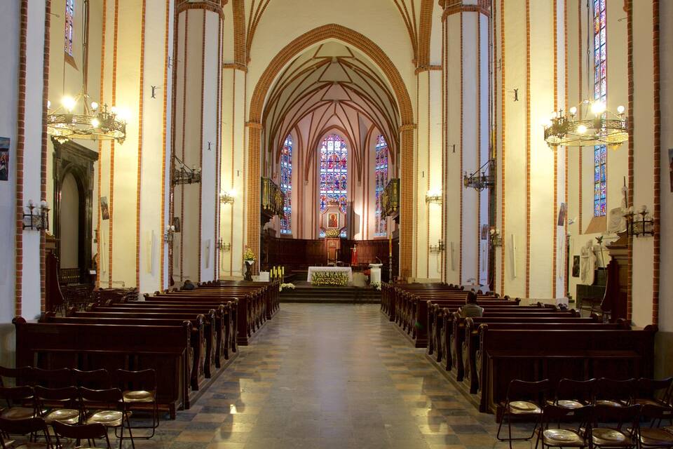 Interior de iglesia con techos altos abovedados, vidrieras de colores y hileras de bancas.