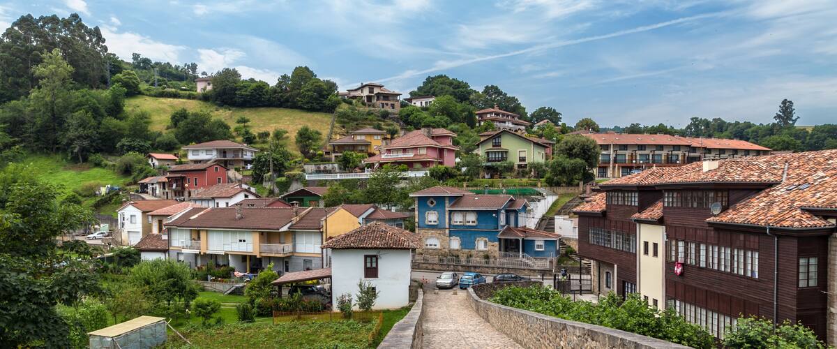 A hillside village with terracotta-roofed houses, a stone wall, and lush greenery.