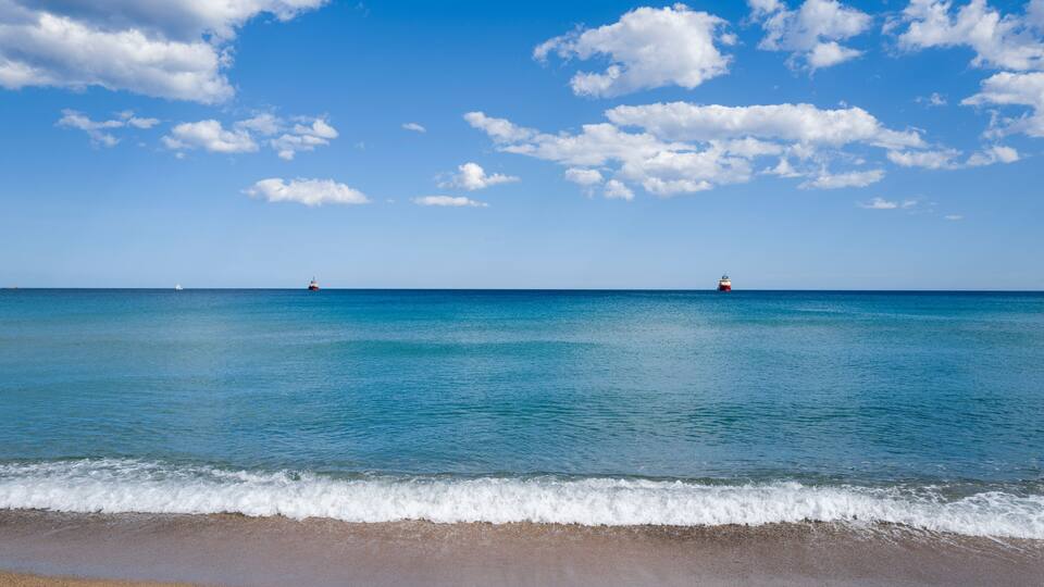 A beach with clear blue water and a few boats in the distance.