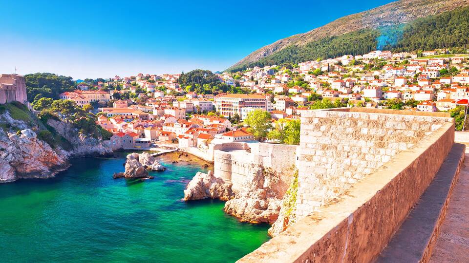 A coastal town with a historic fortification, clear turquoise waters, and a hilly backdrop.