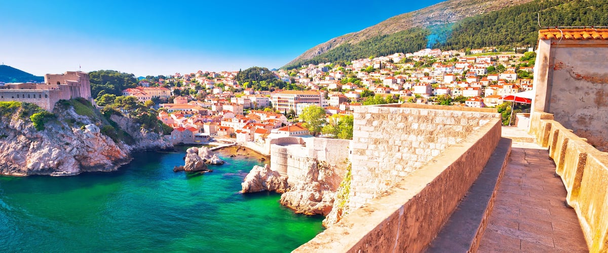 A coastal town with a historic fortification, clear turquoise waters, and a hilly backdrop.