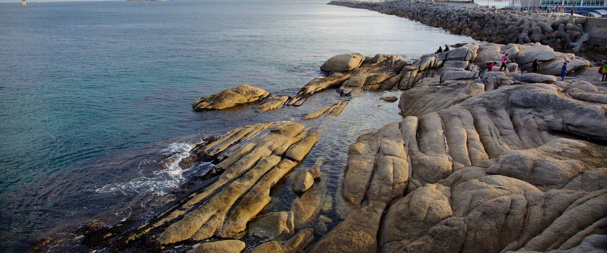A rocky coastline with people walking along a sea wall.