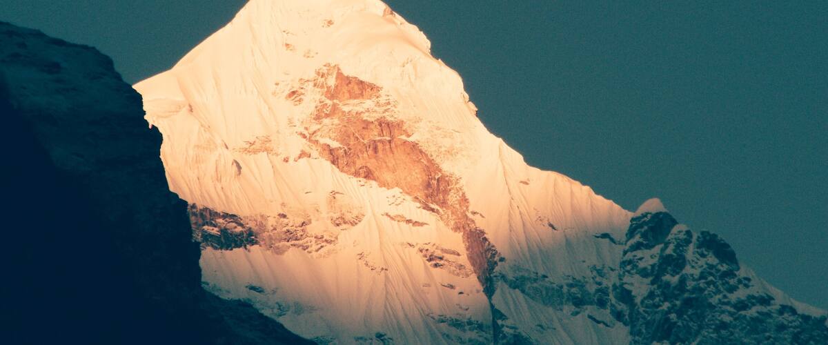 A snow-covered mountain peak with a sharp summit and rugged terrain.