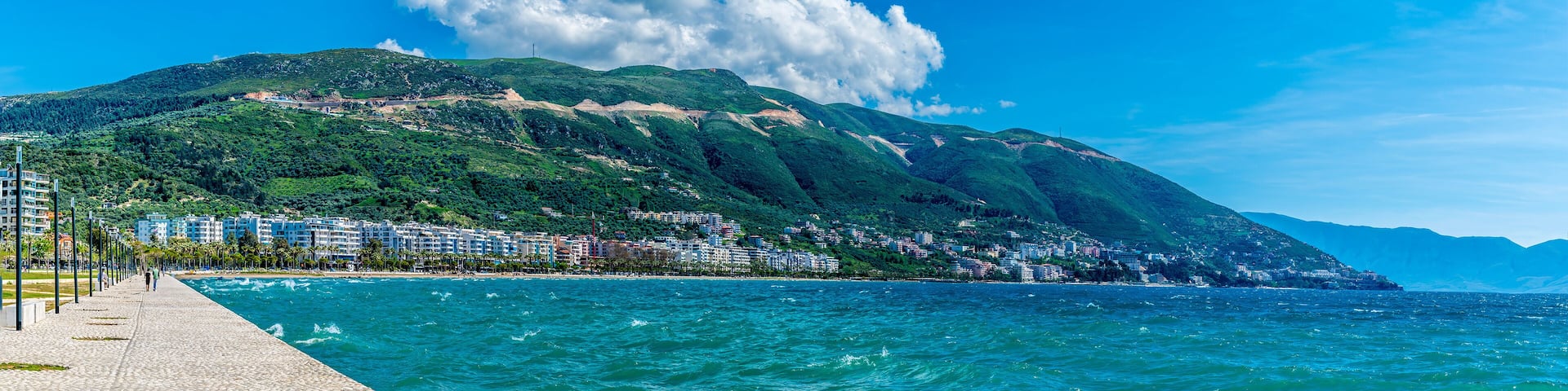 A coastal city with a mountain backdrop, a beach, and a promenade.