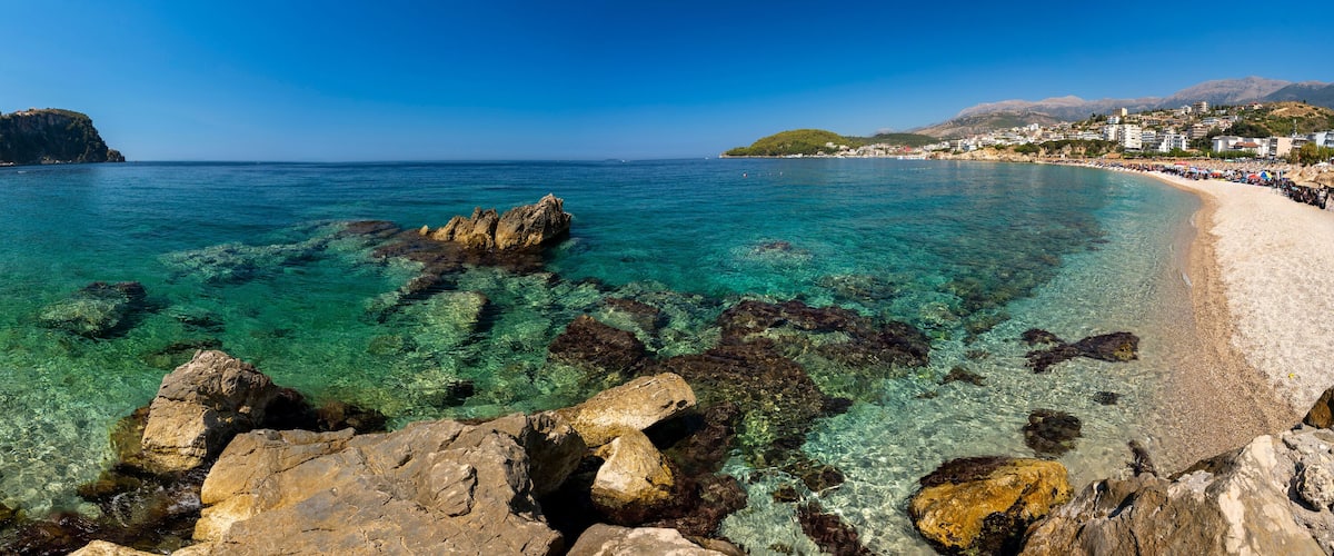 A coastal town with clear turquoise waters, rocky shoreline, and buildings on the hills.