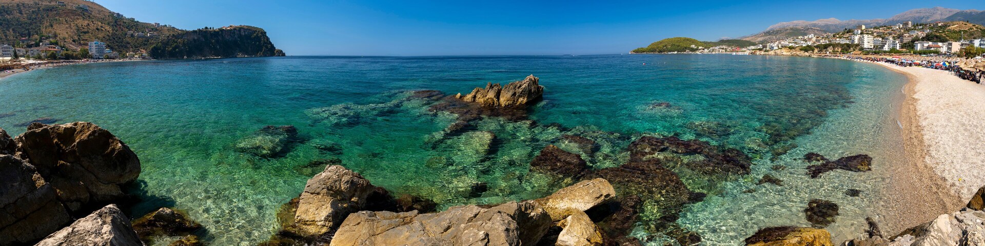 A coastal town with clear turquoise waters, rocky shoreline, and buildings on the hills.