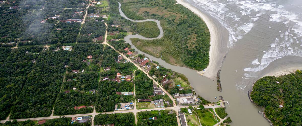 An aerial view of a coastal town with a river, beach, and dense greenery.