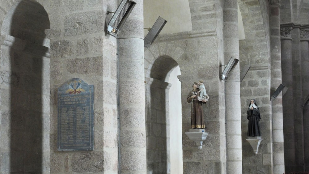 L’intérieur d’une église, avec ses colonnes de pierre, ses bancs en bois et une statue représentant une figure religieuse.