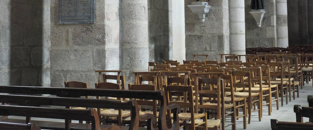 An interior of a church with stone columns, wooden pews, and a statue of a religious figure.