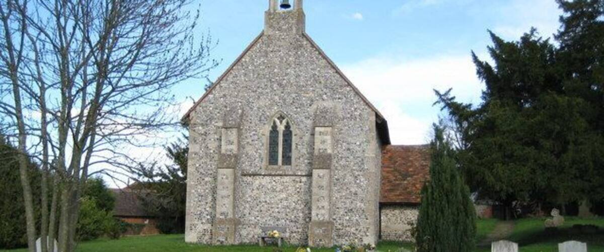 A stone church with a bell tower, surrounded by a cemetery with headstones and a well-maintained lawn.
