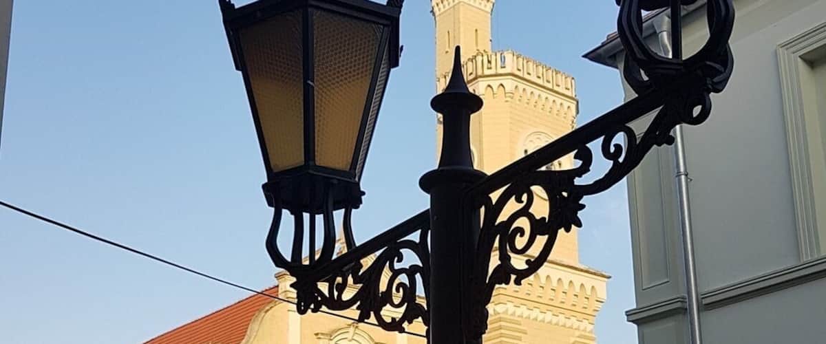 A street lamp with ornate metalwork, a cobblestone square, and a historic building with a tower in the background.