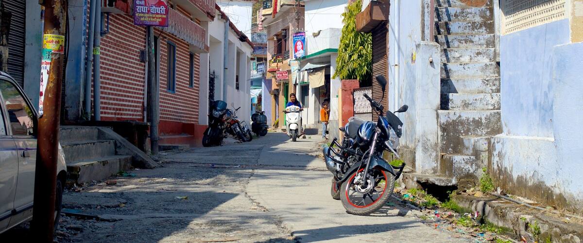 A narrow street lined with buildings, some with signs and posters, and a motorcycle parked on the side.