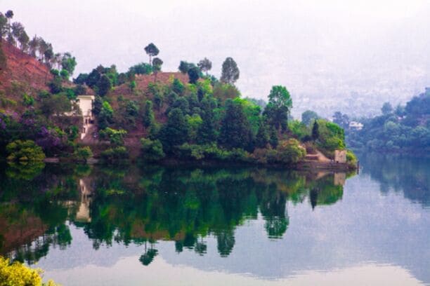 A calm lake with reflections of trees and a building on the shore.